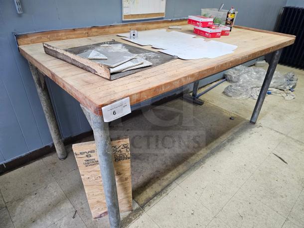 Wood top work table with metal legs, showing signs of use. Features an attached backsplash and visible item label "6 qty".