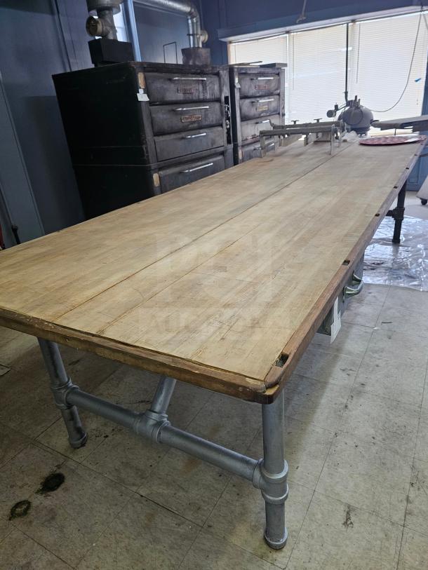 12ft wood top work table with metal pipe legs, showing signs of wear. Ideal for industrial or workshop use.