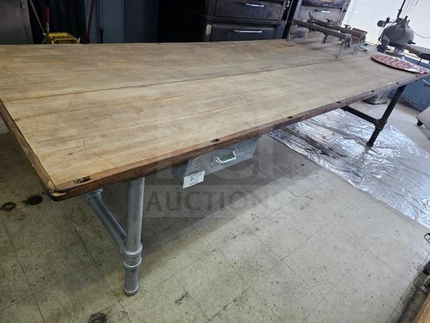 12ft wood top work table with metal pipe legs, good condition, equipped with a drawer beneath.