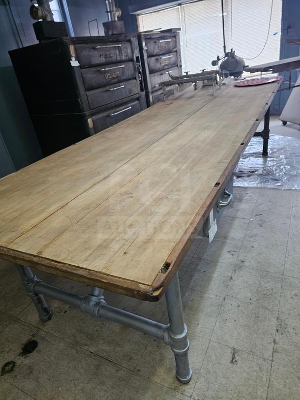 12Ft wood top work table with metal pipe legs, sturdy construction, signs of wear on top, ideal for workshop use.