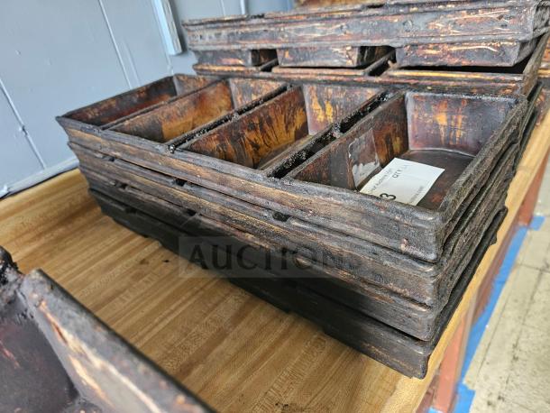 Stack of vintage cast iron baking pans with visible rust, each with rectangular compartments. Numbered tag inside one pan.