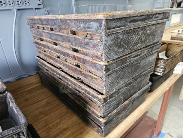 Stack of vintage metal baking pans with rusted patina, featuring textured design and stacked neatly on a wooden table.