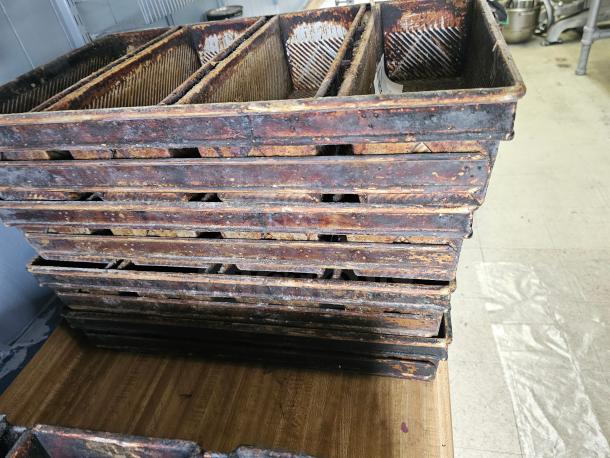 Set of vintage metal baking pans with multiple compartments, showing signs of rust and wear, ideal for industrial-style decor.