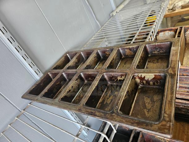 Vintage metal baking pan with 12 rectangular molds, showing signs of wear and patina. Perfect for collectors or vintage kitchenware enthusiasts.