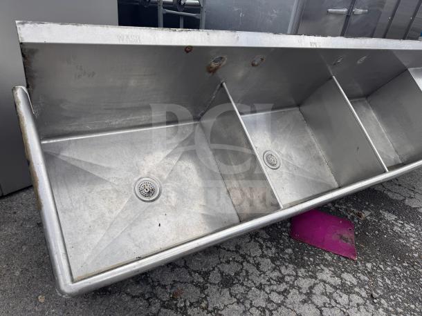 Stainless steel 3-bay sink with "Wash," "Rinse," "Sanitize" labels, used condition, visible wear.