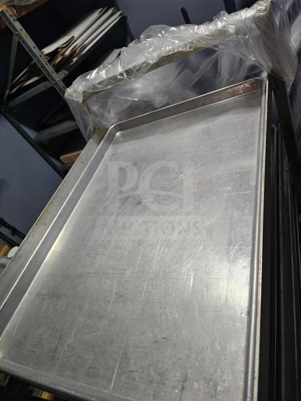 Full-size metallic baking pan with visible scratches, placed on a shelf, covered with clear plastic. Used condition.