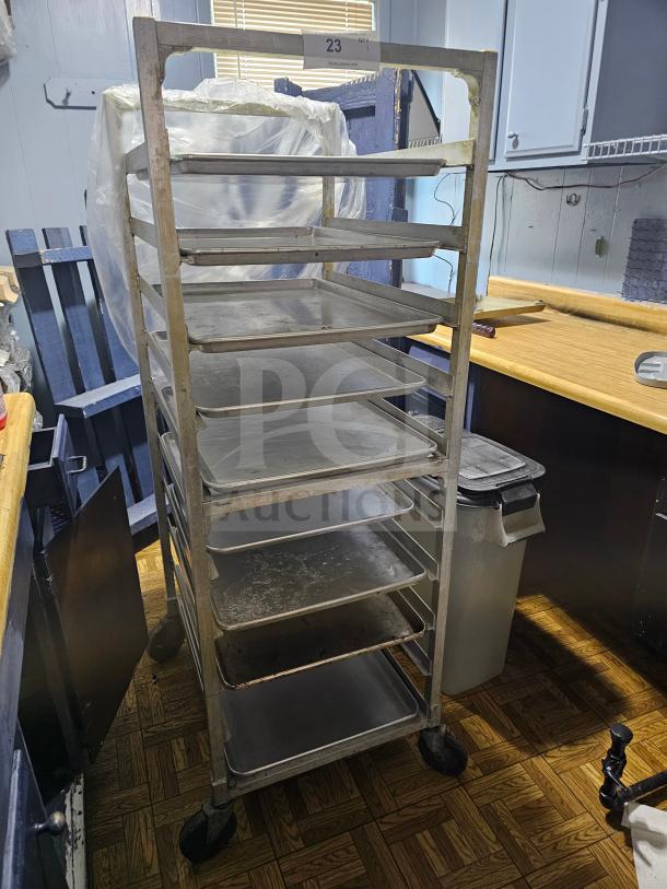Sheet pan rack with multiple shelves, metal frame, on wheels. Used condition. Label reads "23." No contents included.