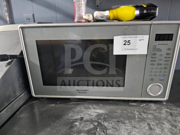 Sharp Carousel microwave, silver finish, digital display, multiple settings. Visible wear, auction tag with "25" label indicated.