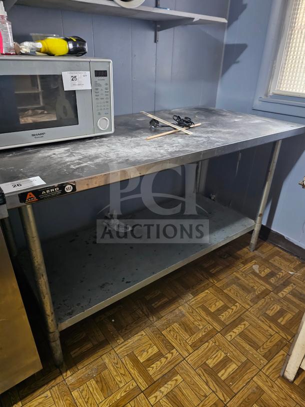 Stainless steel work table with undershelf, signs of wear, AERO label, ideal for kitchen or workshop use.