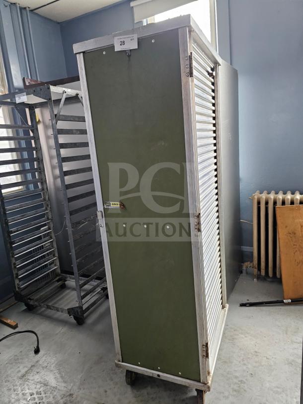Sheet pan rack/cabinet with green panel, metal frame, and rolling wheels. Features serial label "CMF", in used condition.