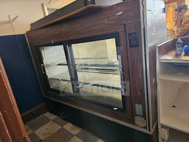 Fogel refrigerated deli display case showing signs of wear and non-functional; features dual glass doors and wood paneling.