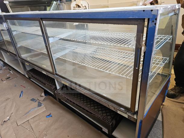 Commercial glass display case with sliding doors, metal frame, multiple shelves, in used condition. Brown base, some tape residue.