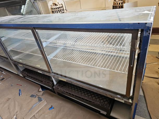 Commercial display case with glass front, sliding doors, and wire shelving. Used condition with visible wear on surfaces.