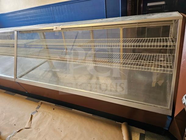 Commercial display case with glass front, metal shelving, and wooden base, showing signs of wear. Tag labeled "34" on top.