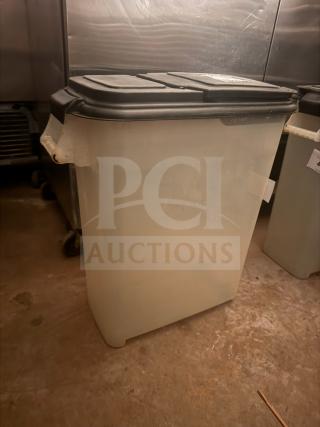 Large translucent storage food container with black lid, industrial setting. Sturdy plastic, moderate wear. Ideal for bulk storage.