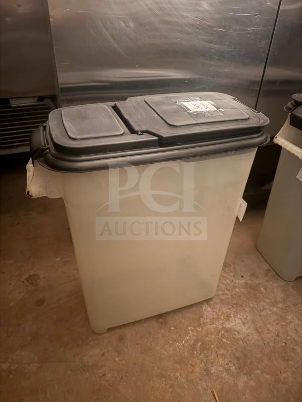 Large plastic storage food container with black lid and label. Used condition, suitable for bulk food storage.