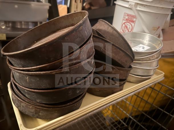 Stacks of round baking pans in varied conditions, predominantly worn and rusted, on a cart in a kitchen setting.