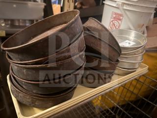 Stacks of round baking pans in varied conditions, predominantly worn and rusted, on a cart in a kitchen setting.