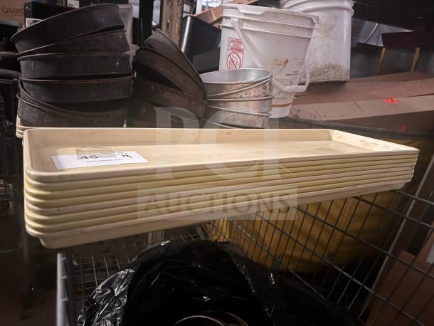 Stack of beige plastic trays, rectangular shape, with slight wear. Auction tag visible with numbers; ideal for catering use.