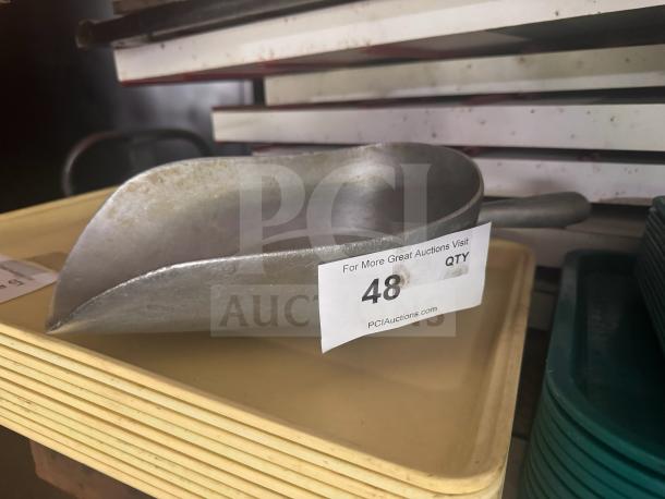 Metal scoop with a handle in used condition, shown on a shelf. Auction label indicates "48 QTY" and website "PCIAuctions.com."