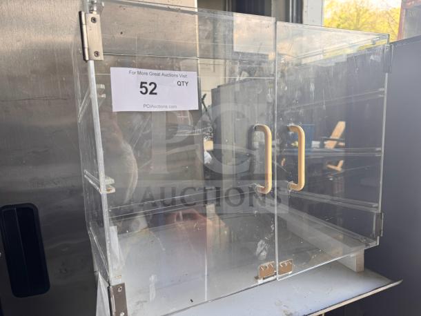 Clear acrylic countertop bakery display case with dual doors, yellow handles, and missing shelves; features label with auction details.