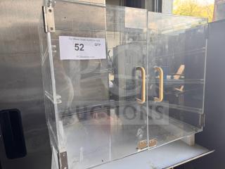 Clear acrylic countertop bakery display case with dual doors, yellow handles, and missing shelves; features label with auction details.