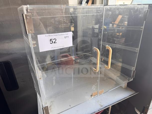 Acrylic countertop bakery display case with clear doors and yellow handles, missing parts, in used condition, auction lot tag visible.