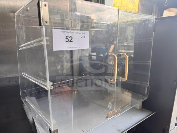 Acrylic countertop bakery display case with double doors, gold handles, and visible shelf brackets; condition shows missing parts.