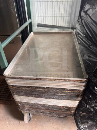 Stack of industrial sheet pans on a wheeled cart, showing wear and oxidation, likely aluminum, used condition.