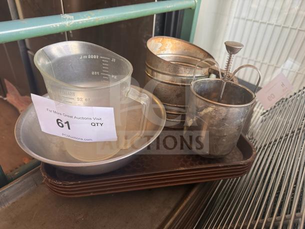 Miscellaneous kitchenware items including a measuring cup, metal sifter, and frother, all placed on a tray. Condition varies.