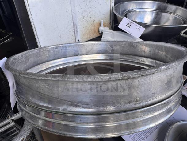 Large aluminum flour sifter in used condition with visible wear, featuring a mesh bottom. Item marked with "64 QTY" tag.