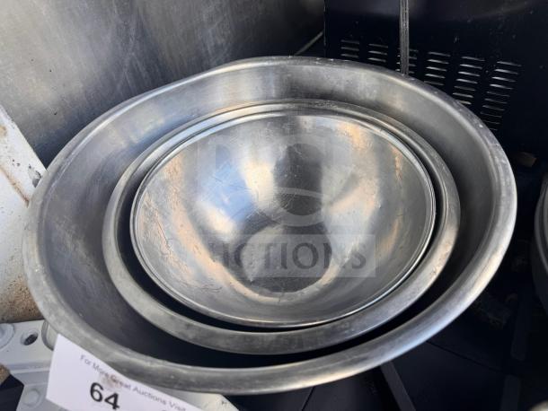 Lot of 3 aluminum mixing bowls, nested for storage, showing wear and scratches. Auction tag with number 64 visible.