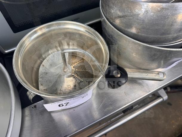 Vintage metal food mill with a hand-crank handle and perforated strainer, in used condition. Auction tag visible: "67 QTY 1".