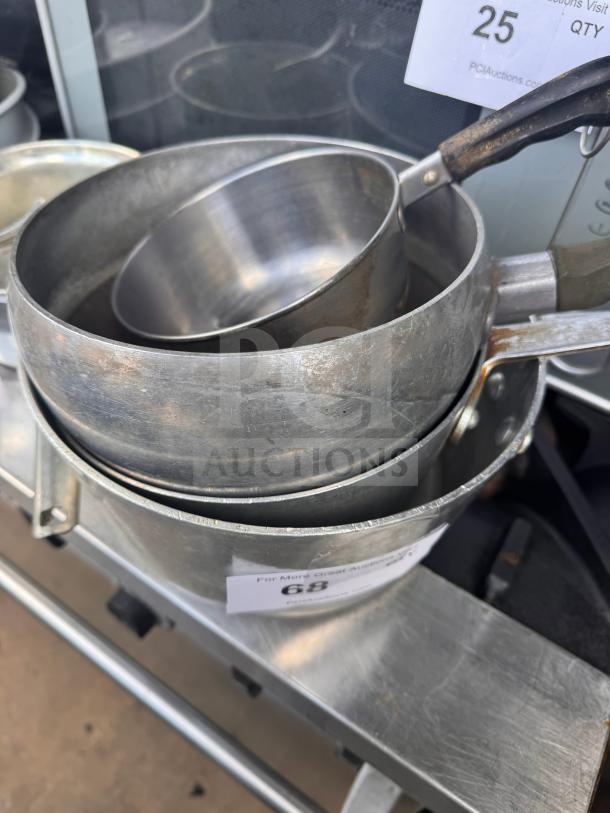 A set of metal saucepans with handles, showing signs of wear. Auction tag with number 68 attached.