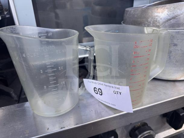 Lot of 2 plastic measuring cups with both metric and standard markings, holding up to 4 cups or 32 oz, slight wear visible.