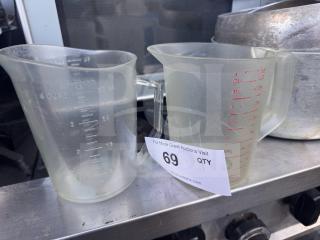 Lot of 2 plastic measuring cups with both metric and standard markings, holding up to 4 cups or 32 oz, slight wear visible.