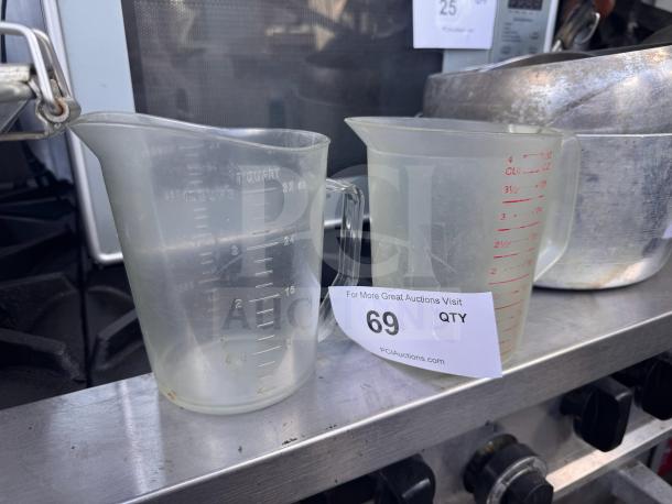 Lot of 2 transparent measuring cups, 1-quart capacity each, with measurement markings. Used condition. Auction tag showing lot number 69.