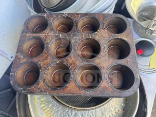 Old aluminum muffin pan with 12 cups, showing signs of wear and rust. Distressed surface, likely vintage.