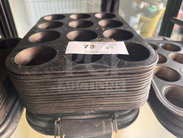 Stacked aluminum muffin pans, showing signs of wear. Auction label reads "73 25 QTY." Suitable for bulk baking.