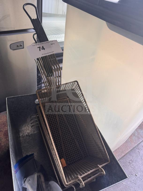 Metal fryer basket with wire mesh design and black handle, in used condition. Auction tag with number 74 visible.