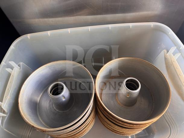 Stack of vintage tube cake pans with central tubes, showing signs of use. Made of metal, stored in a plastic bin.