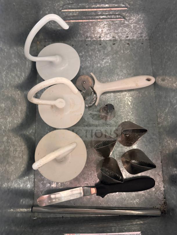 Miscellaneous baking and pastry tools including dough hooks, pastry cutter, spatula, and piping nozzles in a metal tray.