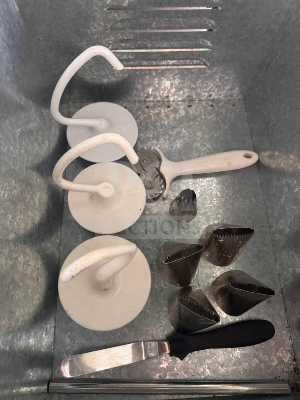 Assorted baking and pastry tools including dough hooks, pastry blender, icing spatula, and piping tips, all in used condition.