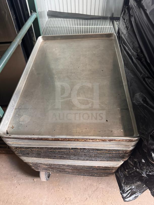 Stack of metal sheet pans in used condition, featuring wear and surface marks, indicative of commercial kitchen use.