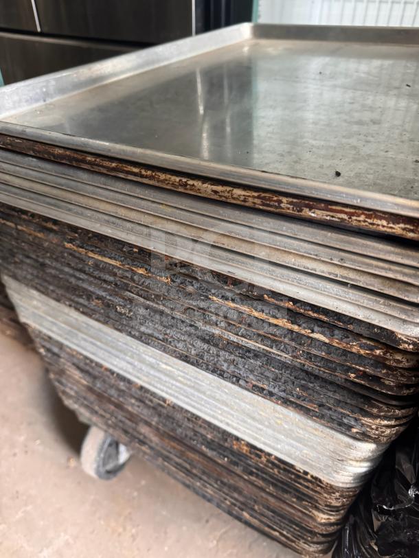 Stack of metal sheet pans with visible wear and discoloration, indicating heavy use.