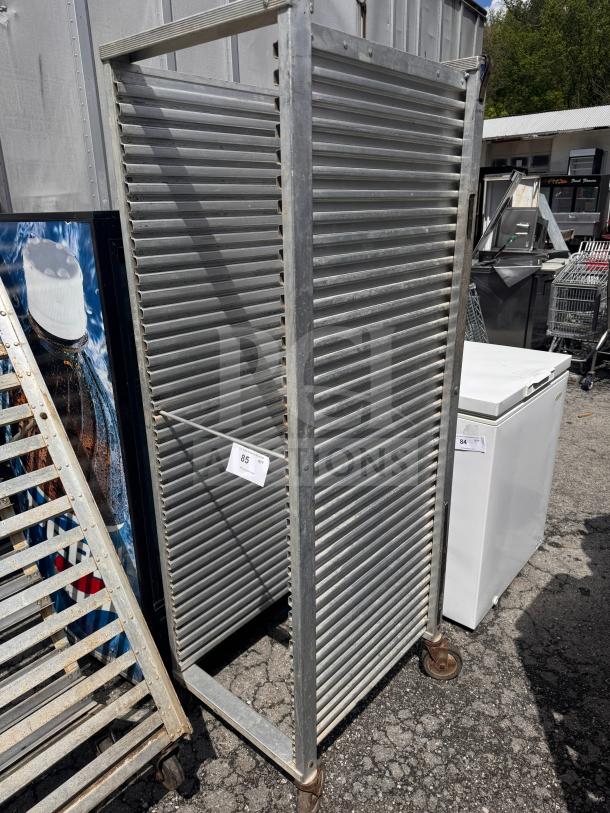 Metal sheet pan rack with multiple horizontal slots, on caster wheels. Slightly weathered. Tag marked "85."