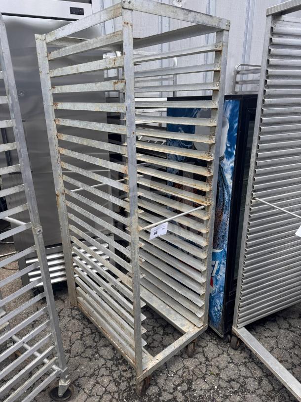 Metal sheet pan rack with multiple slots, rust spots, on casters for easy mobility. Auction tag attached.