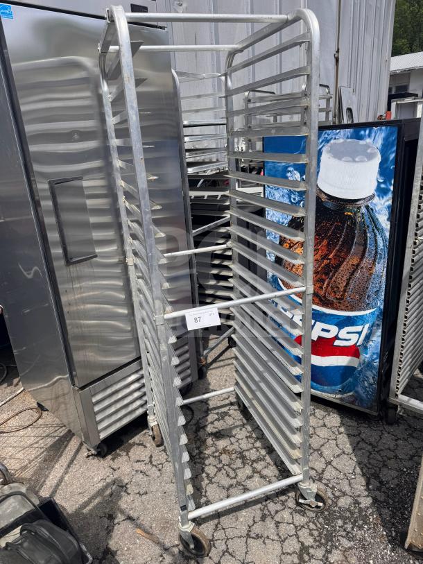 Metal sheet pan rack with multiple shelves, on wheels. Numbered label "87," indicating auction lot. Good condition.