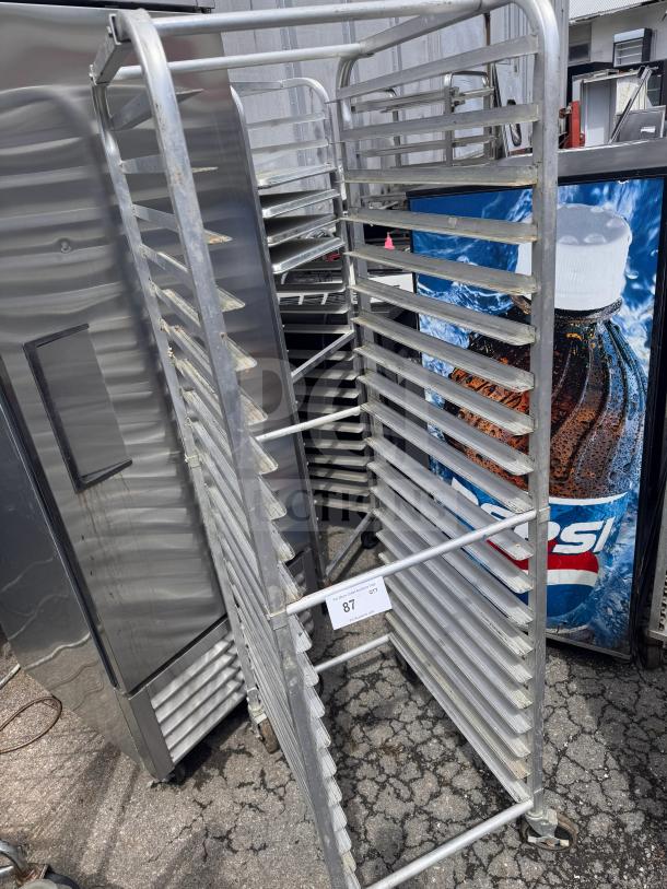 Aluminum sheet pan rack with multiple shelves, used condition, on casters for easy mobility. Tag reads "87 QTY."
