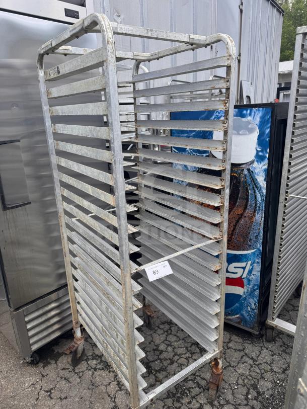 Industrial sheet pan rack with multiple slots, metal construction, visible wear and rust, wheels for mobility. Tag labeled "89."
